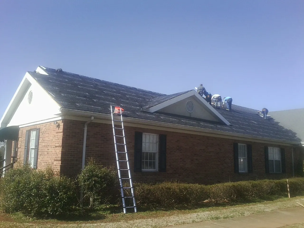 Crew tearing shingles off a brick ranch roof with a ladder set — Metal Roof Repair work by our crew in Blytheville
