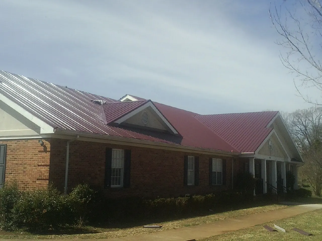 Red metal roof with gabled entries on a long brick building, from a Hail Damage Roof Repair job in Blytheville