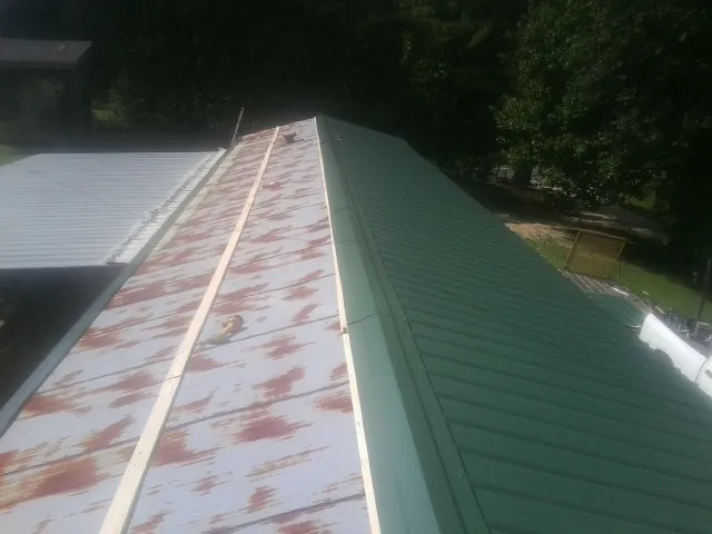 Old rusted panels beside newly installed green metal roofing — Wind Damage Roof Repair by Roofing Brothers in Blytheville