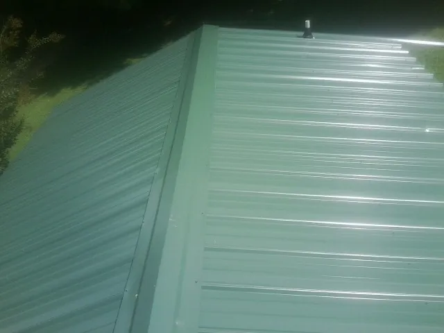 New green metal panels meeting at the ridge of a roof — Flat Roof Repair work by our crew in Blytheville