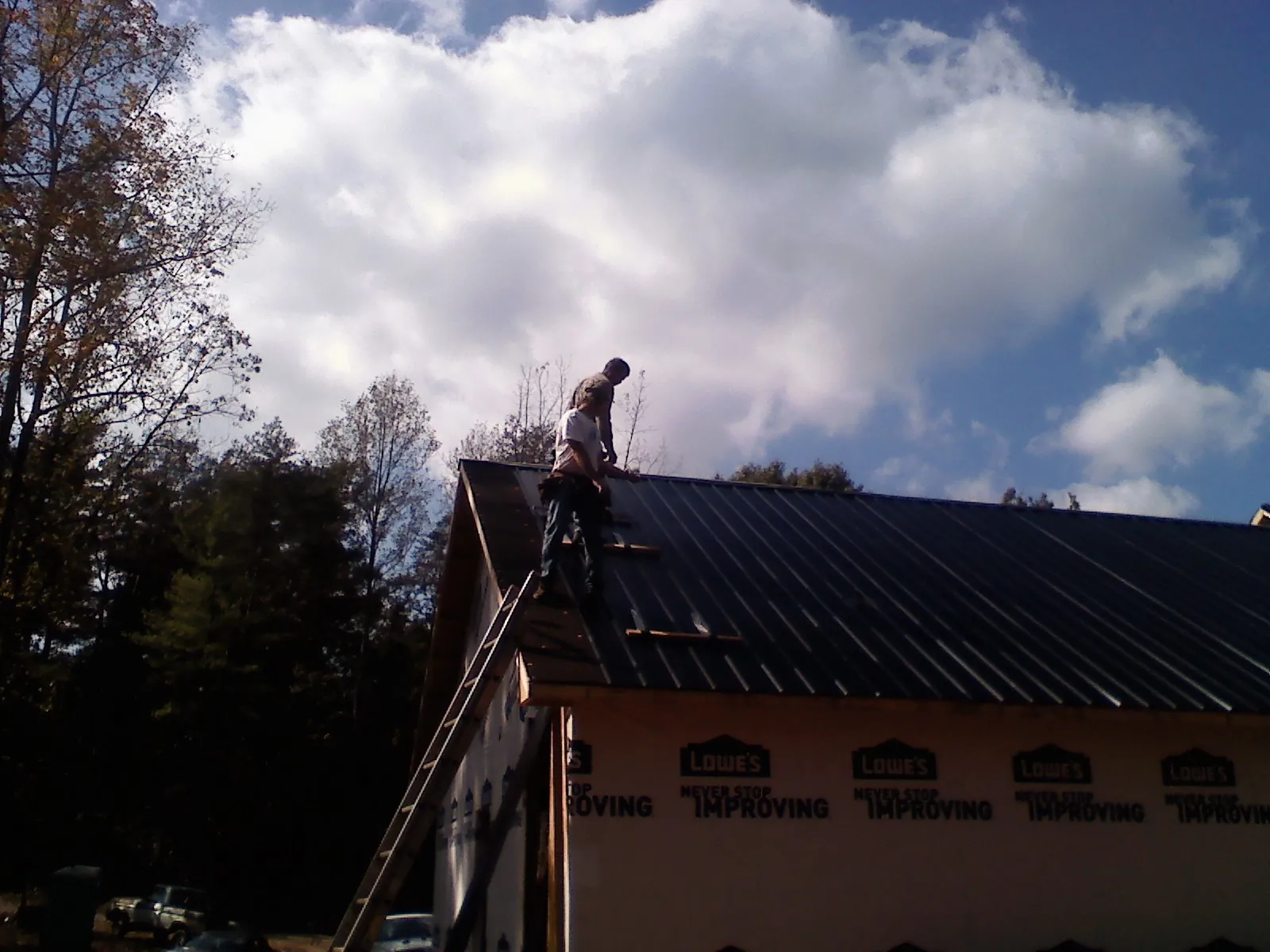 Roofer fastening dark metal panels high against a cloudy sky, from a Roof Inspection job in Blytheville