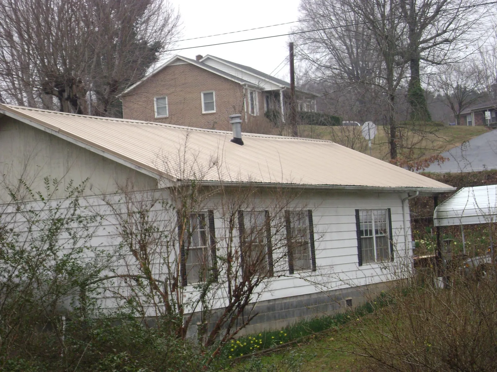 Tan metal roof on a white sided house set into a hillside — Commercial Roofing by Roofing Brothers in Blytheville
